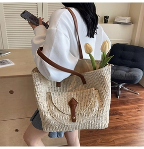 Detail of woven straw tote bag with brown leather trim and front pocket on shoulder