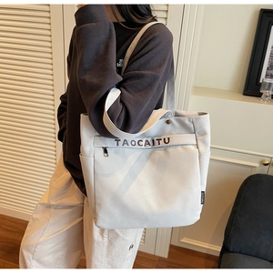 Close-up of cream canvas tote bag featuring brown TAOCAITU lettering and front zipper pocket