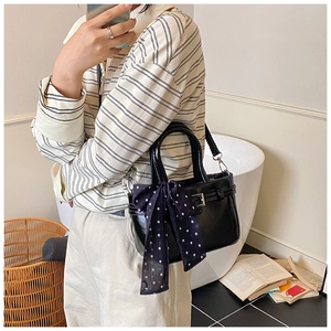 Close-up of black crossbody bag with blue polka dot bow and silver buckle detail