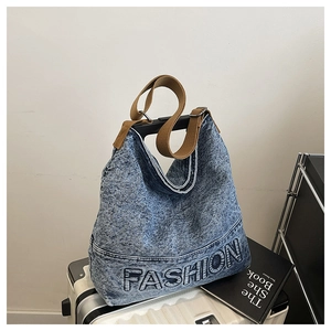 Detail of denim hobo bag with Fashion text and adjustable wide shoulder strap on luggage