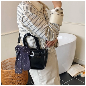 Detail of black patent leather crossbody bag with a polka dot silk scarf on handle