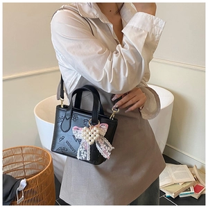 Detail of black embossed PU bucket bag with lace bow and pearl charm on a model