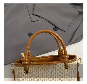 Detail of woven beige handbag featuring brown leather handles and golden hardware