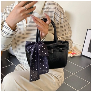 Detail of black patent leather handbag with silver buckle and polka dot silk scarf