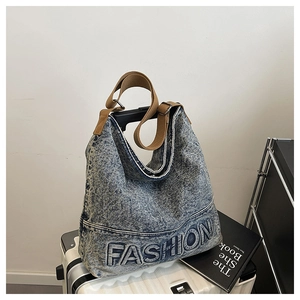 Detail of blue denim hobo bag with embossed FASHION logo on a white suitcase