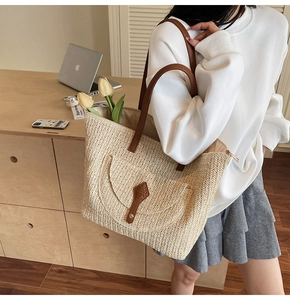 Detail of woven straw tote bag featuring brown leather straps and large capacity for summer