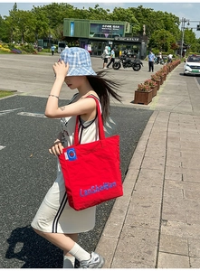 Détail du sac cabas en nylon rouge avec lettrage contrasté bleu et anses robustes