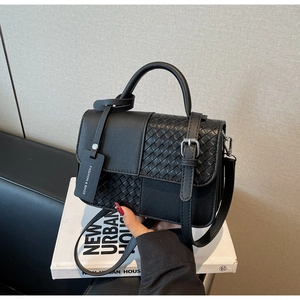 Detail of black crossbody bag featuring smooth and woven textures with silver hardware
