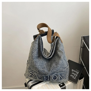 Detail of blue washed denim hobo bag with FASHION lettering and brown fabric shoulder strap