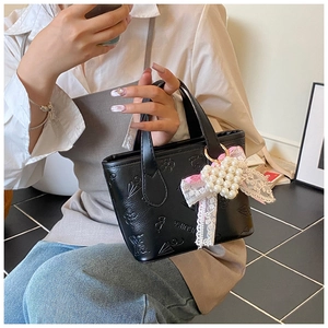 Detail view of butterfly embossed black leather bucket bag with lace pearl bow handle