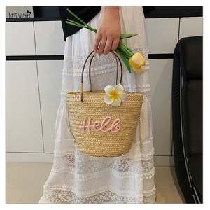 Detail der Strohtasche mit rosa Hello-Stickerei und tropischem Frangipani-Anhänger