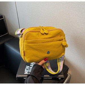 Détail d'un sac bandoulière en nylon jaune avec trois compartiments zippés et sangle jacquard