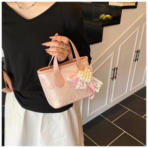 Detailed close-up of pink bucket bag with butterfly embossing and pearl lace heart charm