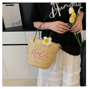 Detail der Strohhandtasche mit Hello-Stickerei, Kunstblume und Kordelzugverschluss