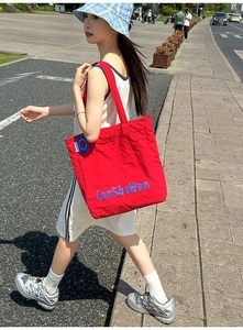 Gros plan d'un sac cabas en nylon rouge avec broderie bleue et détails de texture