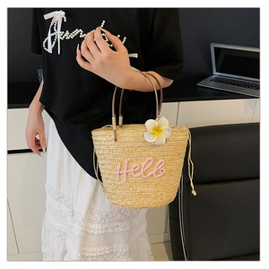 Detail der Strohtasche mit rosa Hello-Stickerei und einer dekorativen Frangipani-Blüte