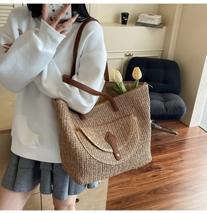 Detail of hand-woven straw tote bag showing brown faux leather strap and buckle closure