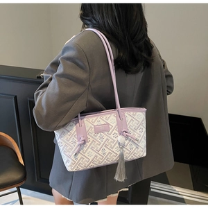 Detail der lila Schultertasche mit geometrischem Muster, Quaste und Logo am Model