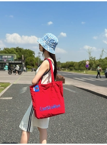 Photo en extérieur d'un sac cabas en nylon rouge avec broderie bleue sur le modèle