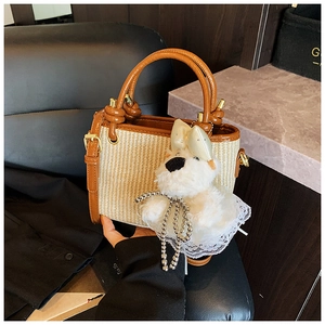 Détail du sac seau en paille tressée avec lanières en cuir marron et charm de chien en peluche