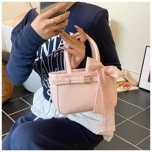 Detail of light pink square bag with a large polka dot silk bow on the top handle