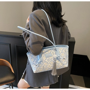 Detail einer hellblauen Schultertasche mit Blumenstickerei und grauem Quasten-Anhänger
