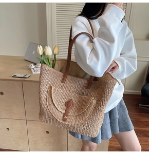 Detail of handwoven straw tote bag featuring leather shoulder straps and vintage front pocket