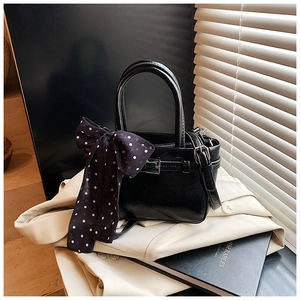 Detail of black lychee-textured leather handbag with silver buckle and polka dot scarf