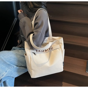 Detail of a large cream canvas tote bag with front zipper pocket and side water bottle holder