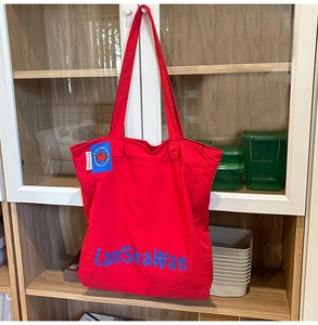 Détail du grand sac cabas en nylon rouge avec lettrage bleu et écusson pomme brodé