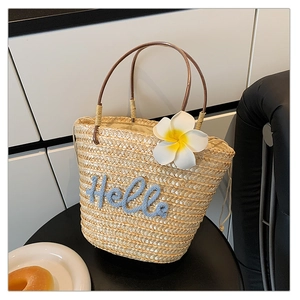 Detailansicht der Strohtasche mit blauem Hello-Schriftzug und dekorativer Frangipani-Blüte