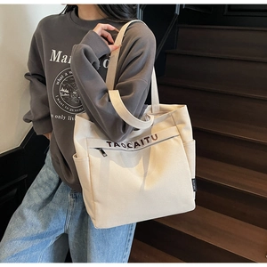 Detail of canvas tote bag with side pockets, front zipper pocket and letter print