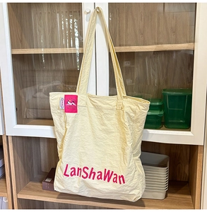 Détail du sac fourre-tout en nylon crème avec lettrage rouge dans un décor minimaliste