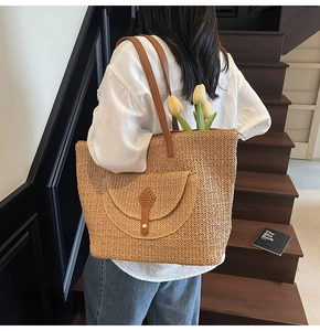 Close-up of woven straw tote bag featuring a leather pocket with metal buckle detail
