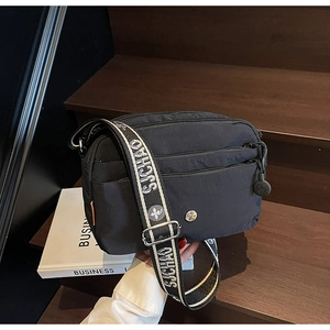Détail du sac bandoulière en nylon noir avec large sangle à logo sur un escalier en bois