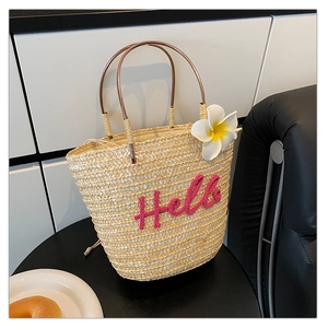 Detailansicht der beigen Strohtasche mit rosa Hello-Stickerei und Frangipani-Blüte