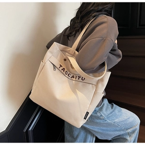 Side view of beige canvas tote bag with shoulder strap showing large capacity on model