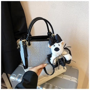 Détail du sac seau tissé avec garniture en cuir verni noir et breloque chiot