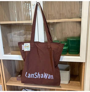 Détail du grand sac cabas en nylon marron foncé avec texte violet et étiquette tissée blanche