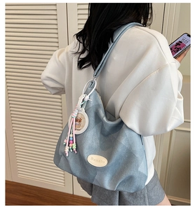 Détail du sac hobo bleu clair avec écusson en cuir Banatu et breloque à pompon en perles
