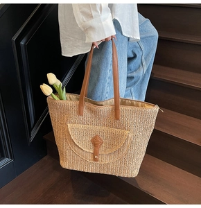 Detail of woven straw tote bag with brown leather straps and front pocket on stairs