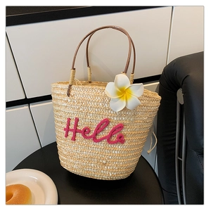 Detail der Strohtasche mit rosa Hello-Stickerei und Plumeria-Blumenanhänger