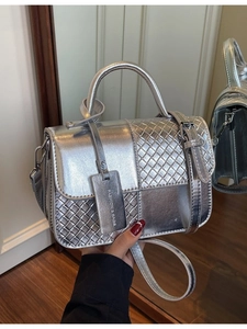 Silver metallic crossbody bag with woven texture and top handle shown in a mirror