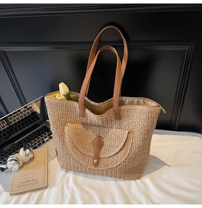 Close-up of straw woven tote bag featuring brown leather pocket and secure zipper closure
