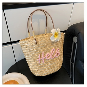 Detail der handgewebten Strohtasche mit rosa Hello-Stickerei und Blumenakzenten