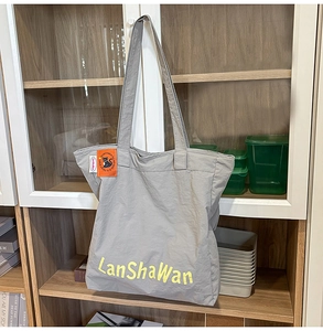 Vue détaillée du sac cabas en nylon gris avec logo jaune et étiquette de chat orange