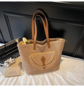 Close-up of a woven straw tote bag with brown leather handles and a front pocket detail