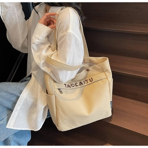 Dettaglio della borsa tote in tela beige con tasca a zip ed etichetta del marchio