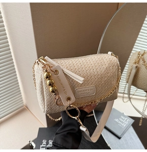 Détail du sac cylindre tissé beige avec chaîne dorée et décoration de glands blancs