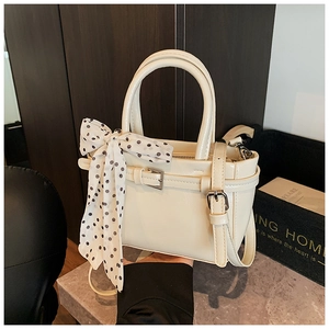 Detail view of cream white shoulder bag with decorative polka dot scarf and twin buckle straps